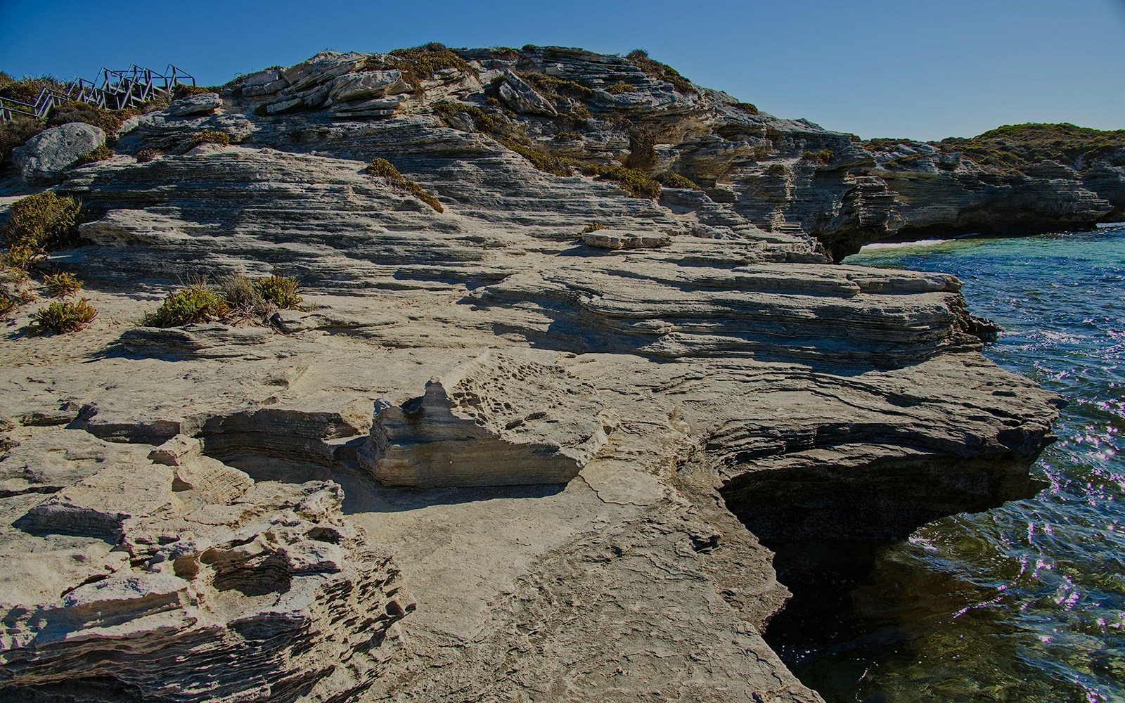 Rocky shoreline at Henrietta Rocks, Rottnest Island, with clear blue water and rugged cliffs.
