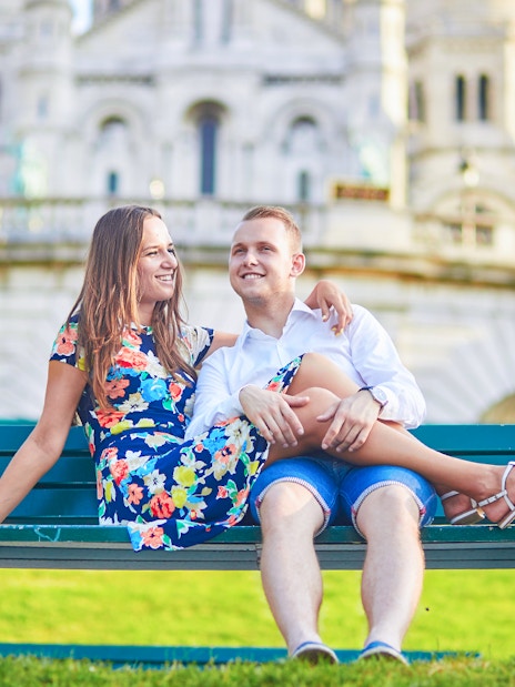 Couple sitting on a bench in front of Sacré-Cœur Basilica, Montmartre, Paris.