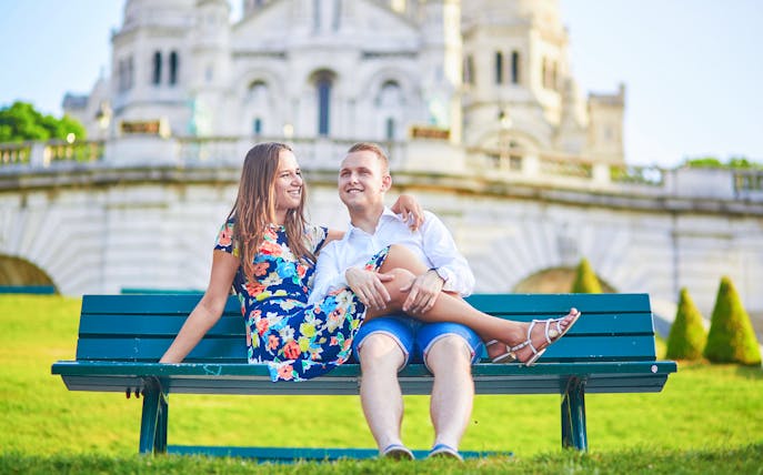 Couple sitting on a bench in front of Sacré-Cœur Basilica, Montmartre, Paris.