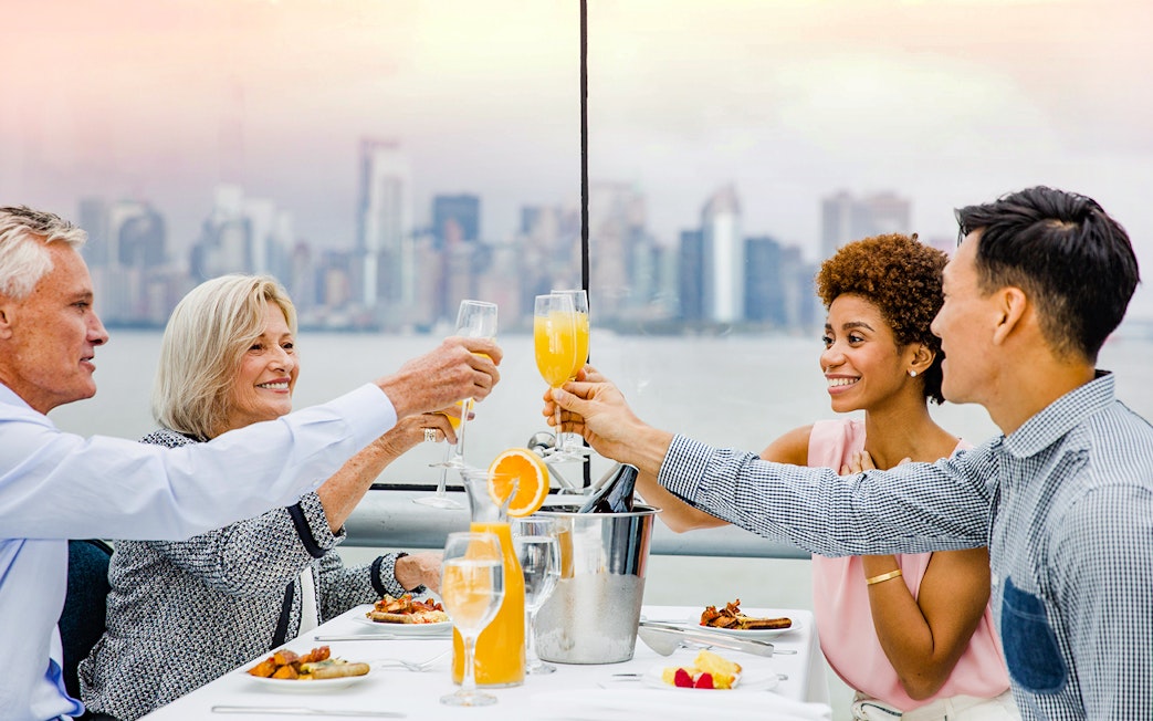 Passengers enjoying cocktails on Bateaux Brunch Cruise with city skyline in background.