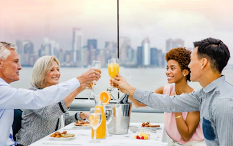 Passengers enjoying cocktails on Bateaux Brunch Cruise with city skyline in background.