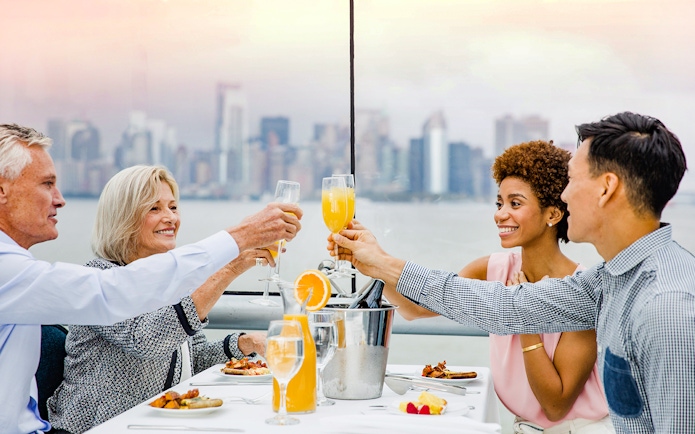 Passengers enjoying cocktails on Bateaux Brunch Cruise with city skyline in background.