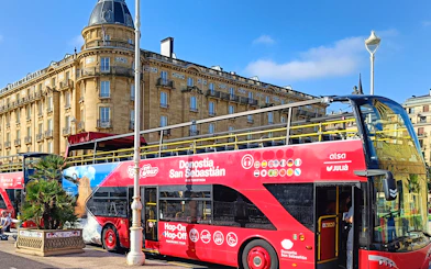 Hop-on hop-off tour bus in front of historic building in San Sebastian.