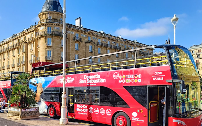 Hop-on hop-off tour bus in front of historic building in San Sebastian.