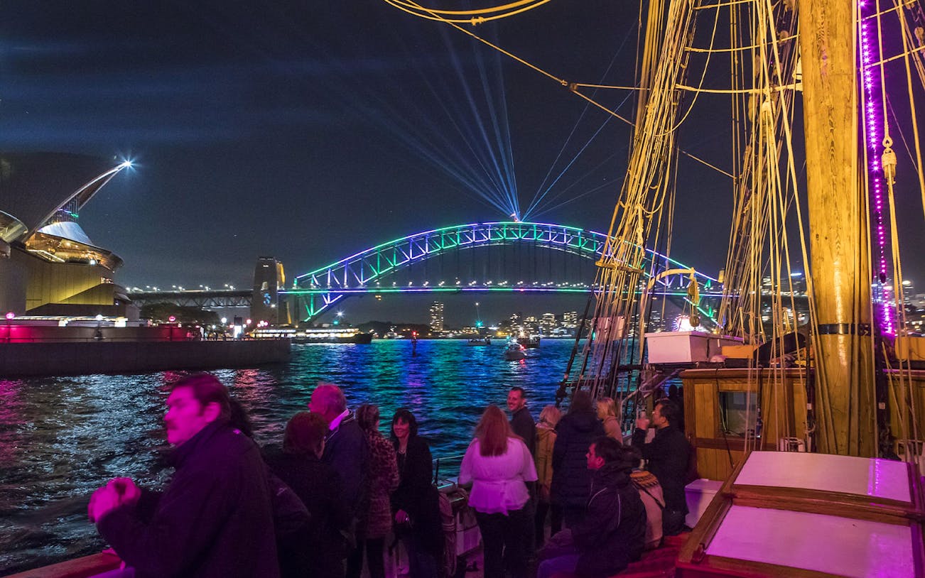Tall ship cruise with people enjoying views of Sydney Harbour Bridge and Opera House during Vivid Sydney.