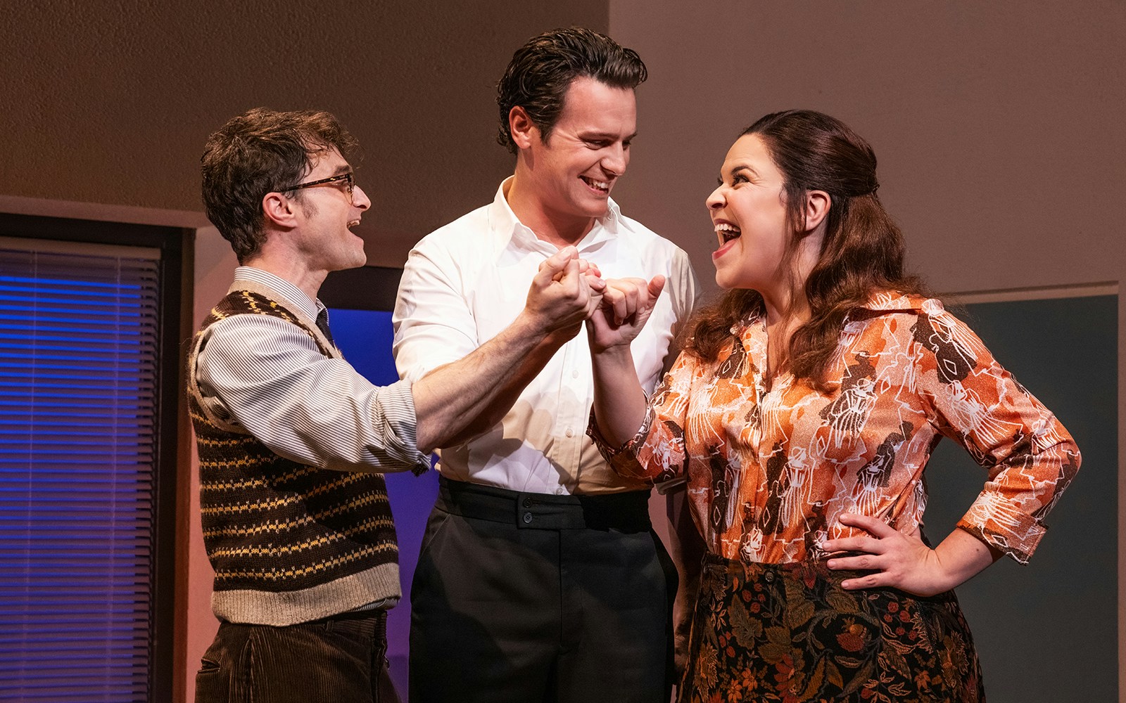 Three actors in a scene from "Merrily We Roll Along," linking hands and smiling.