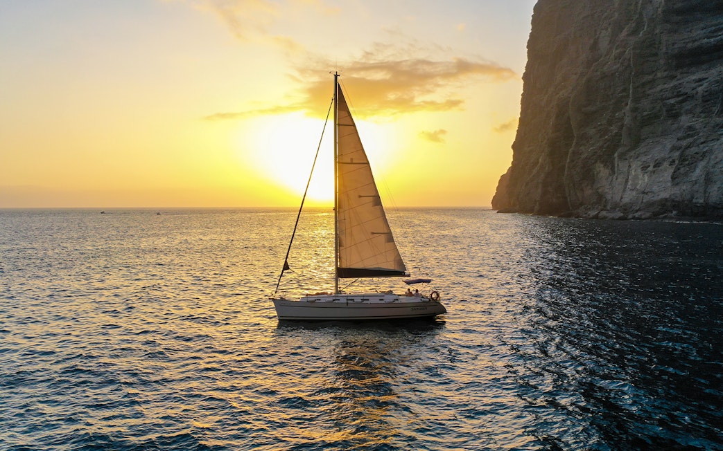 Sailboat cruising at sunset near cliffs during whale and dolphin watching tour.