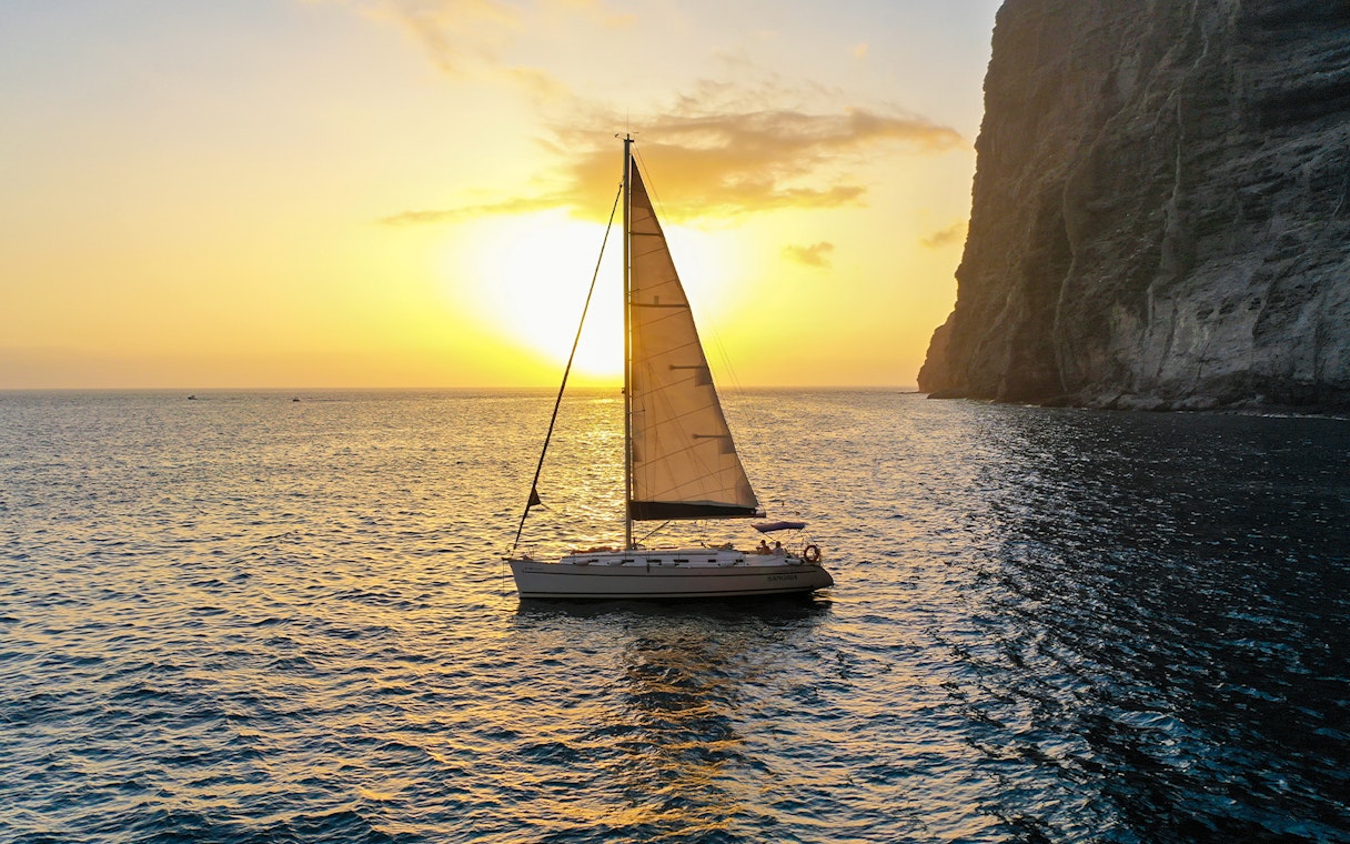 Sailboat cruising at sunset near cliffs during whale and dolphin watching tour.
