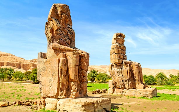 Colossi of Memnon statues in Luxor, Egypt, under a clear blue sky.