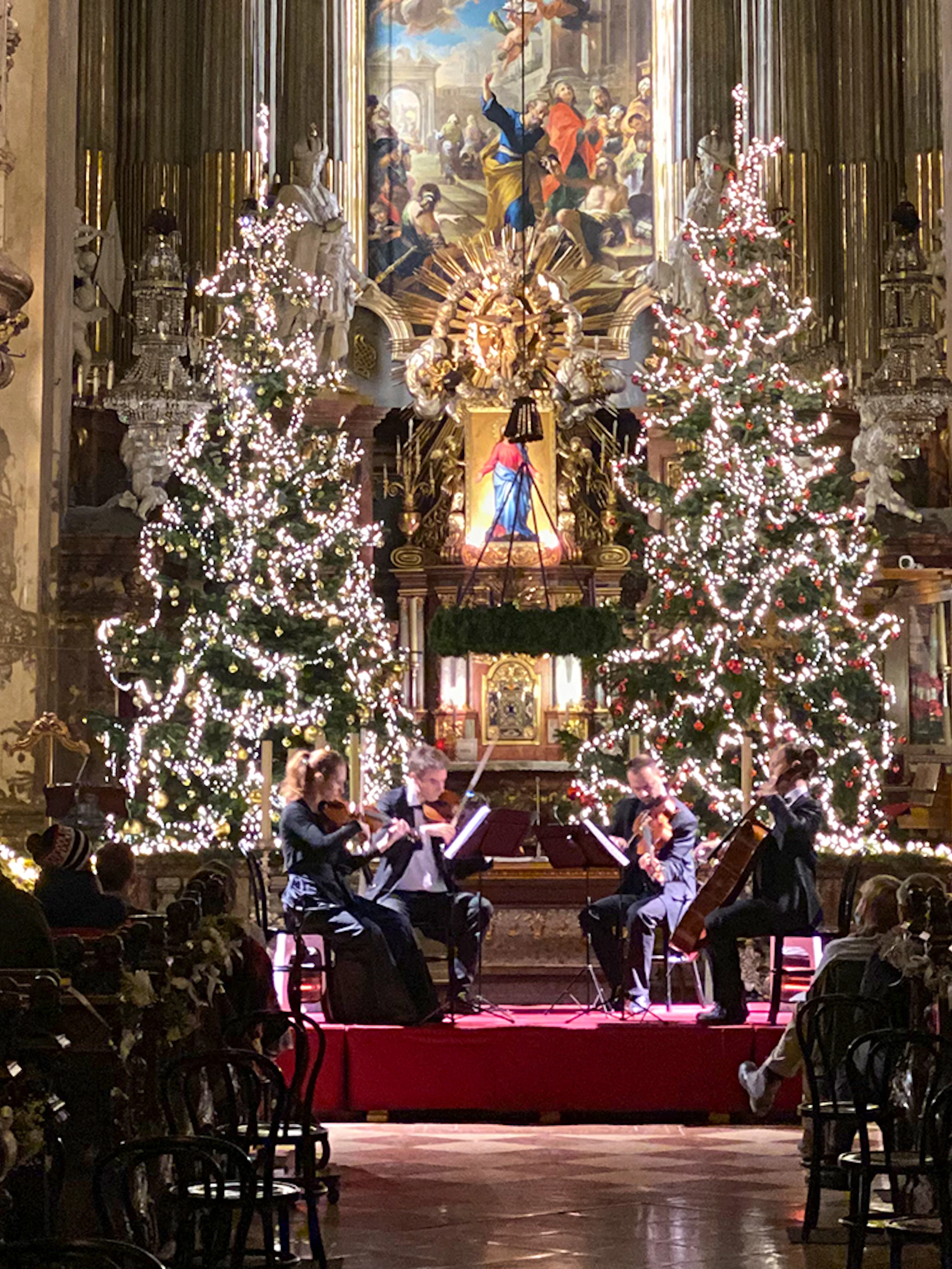 String quartet performing at St. Peter's Church, Vienna, with Christmas trees and festive decor.