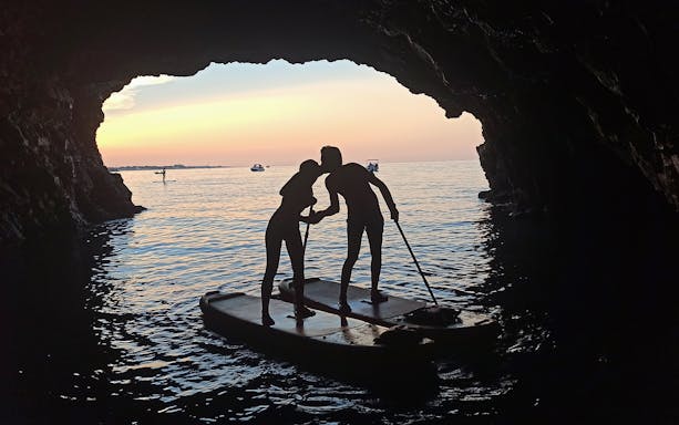Stand-up paddleboarders in a cave at sunset, Polignano a Mare tour.