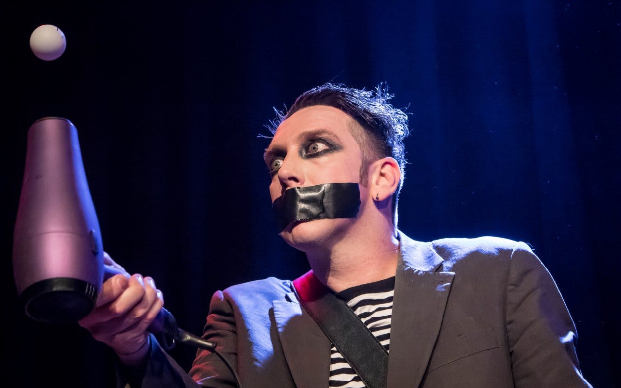 Performer with taped mouth using hairdryer in Tape Face Vegas show.