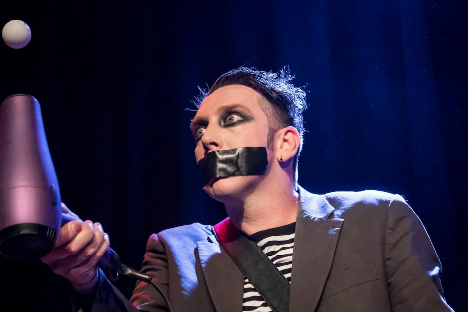 Performer with taped mouth using hairdryer in Tape Face Vegas show.