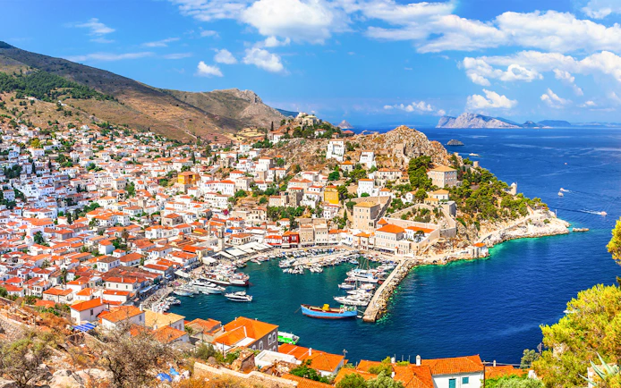 Aerial view of Hydra Island's harbor with boats and hillside houses, Greece.
