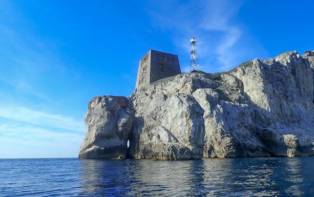 Rocky coastline with a tower and lighthouse at Ieranto Bay, seen from the water during a kayak tour.