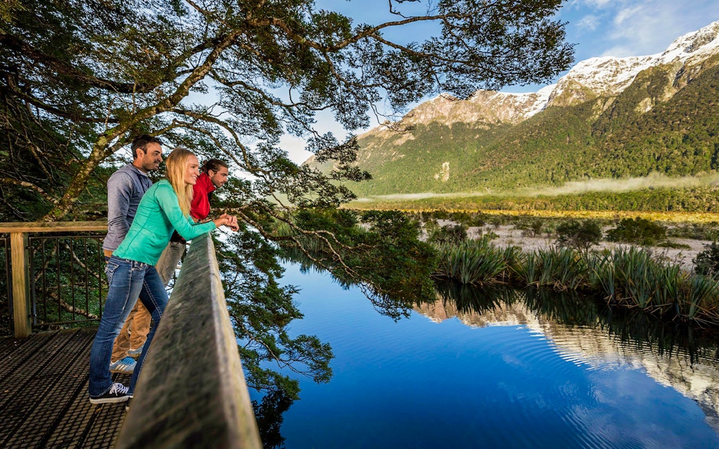 Visitors enjoying the view at Mirror Lakes, New Zealand, with mountains reflected in the water.