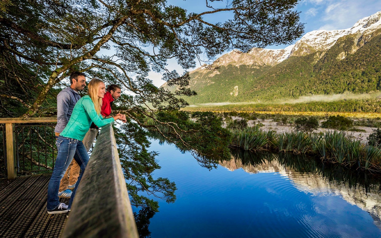 Visitors enjoying the view at Mirror Lakes, New Zealand, with mountains reflected in the water.