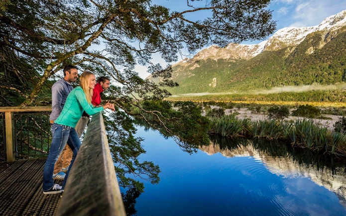 Visitors enjoying the view at Mirror Lakes, New Zealand, with mountains reflected in the water.