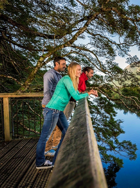 Visitors enjoying the view at Mirror Lakes, New Zealand, with mountains reflected in the water.