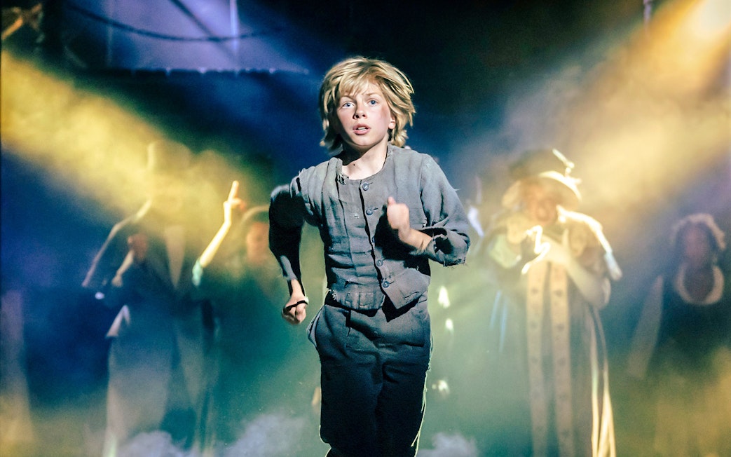 Child actor running on stage during Oliver production with dramatic lighting.