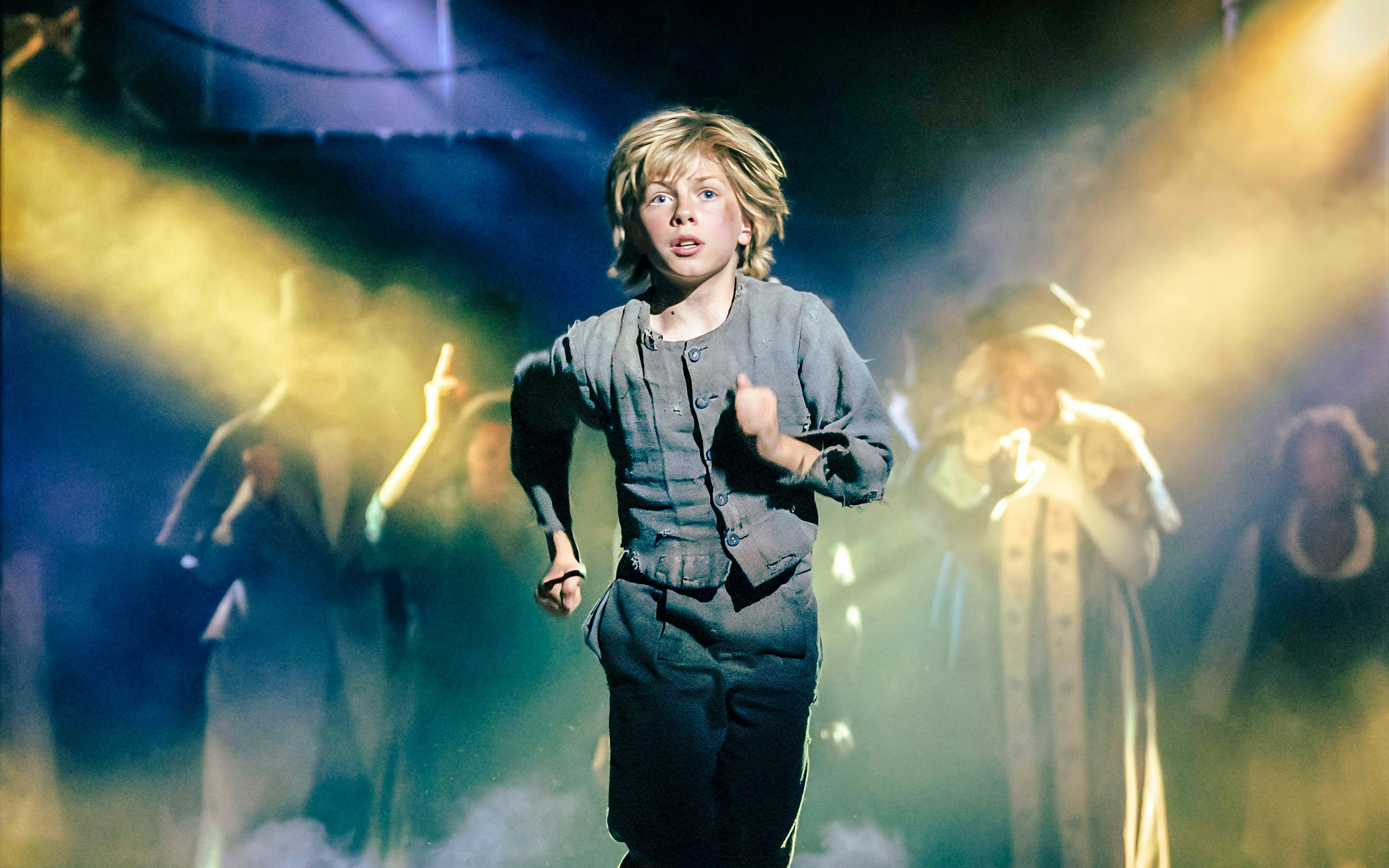 Child actor running on stage during Oliver production with dramatic lighting.