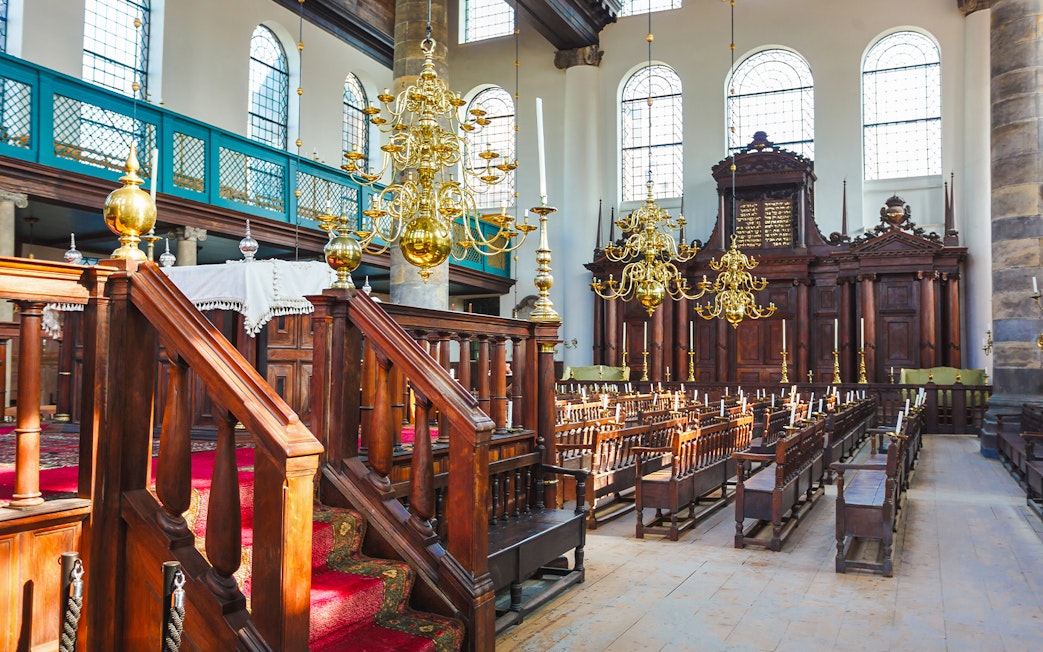 Interior of historic synagogue with wooden pews and chandeliers, part of Anne Frank walking tour.