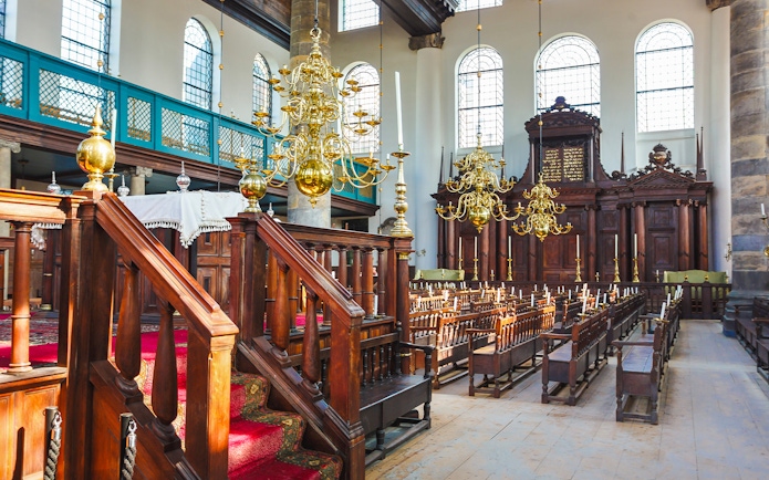 Interior of historic synagogue with wooden pews and chandeliers, part of Anne Frank walking tour.