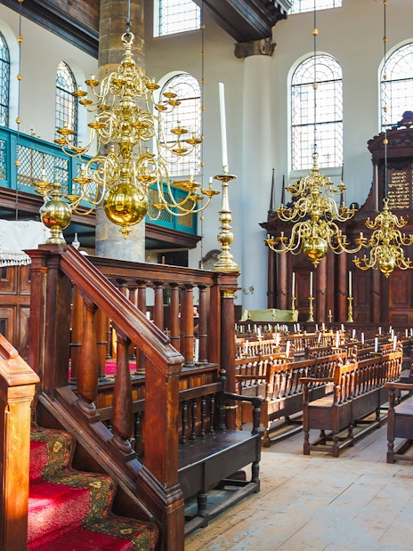 Interior of historic synagogue with wooden pews and chandeliers, part of Anne Frank walking tour.