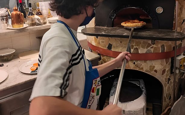 Person placing pizza in a stone oven during a cooking class in Naples.