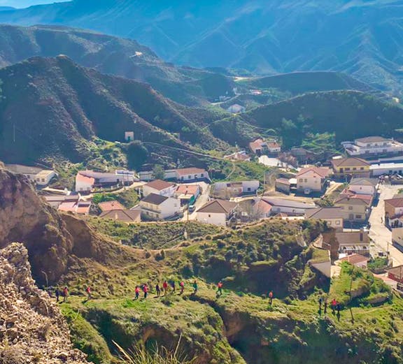 Hikers exploring trails in Geopark Granada with mountainous landscape and village below.