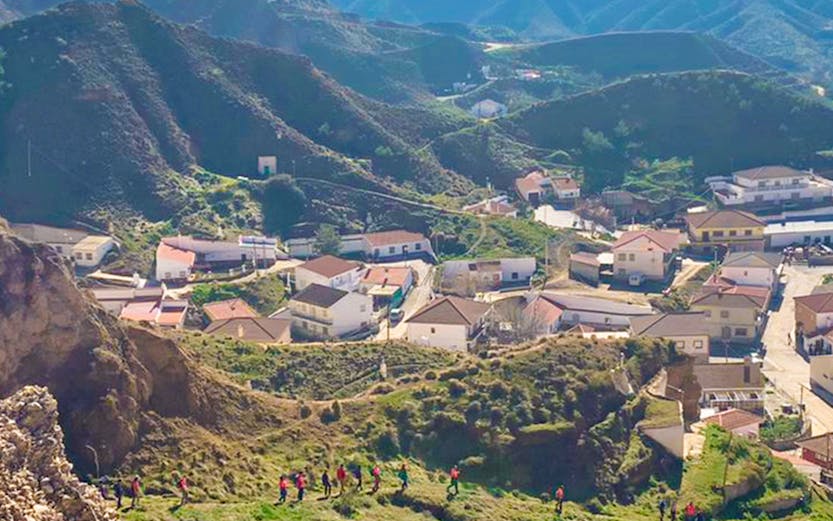 Hikers exploring trails in Geopark Granada with mountainous landscape and village below.