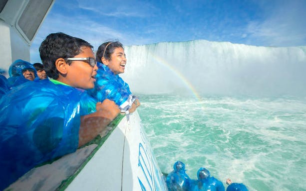 Tourists in blue ponchos on Maid of the Mist boat near Niagara Falls USA with a rainbow.