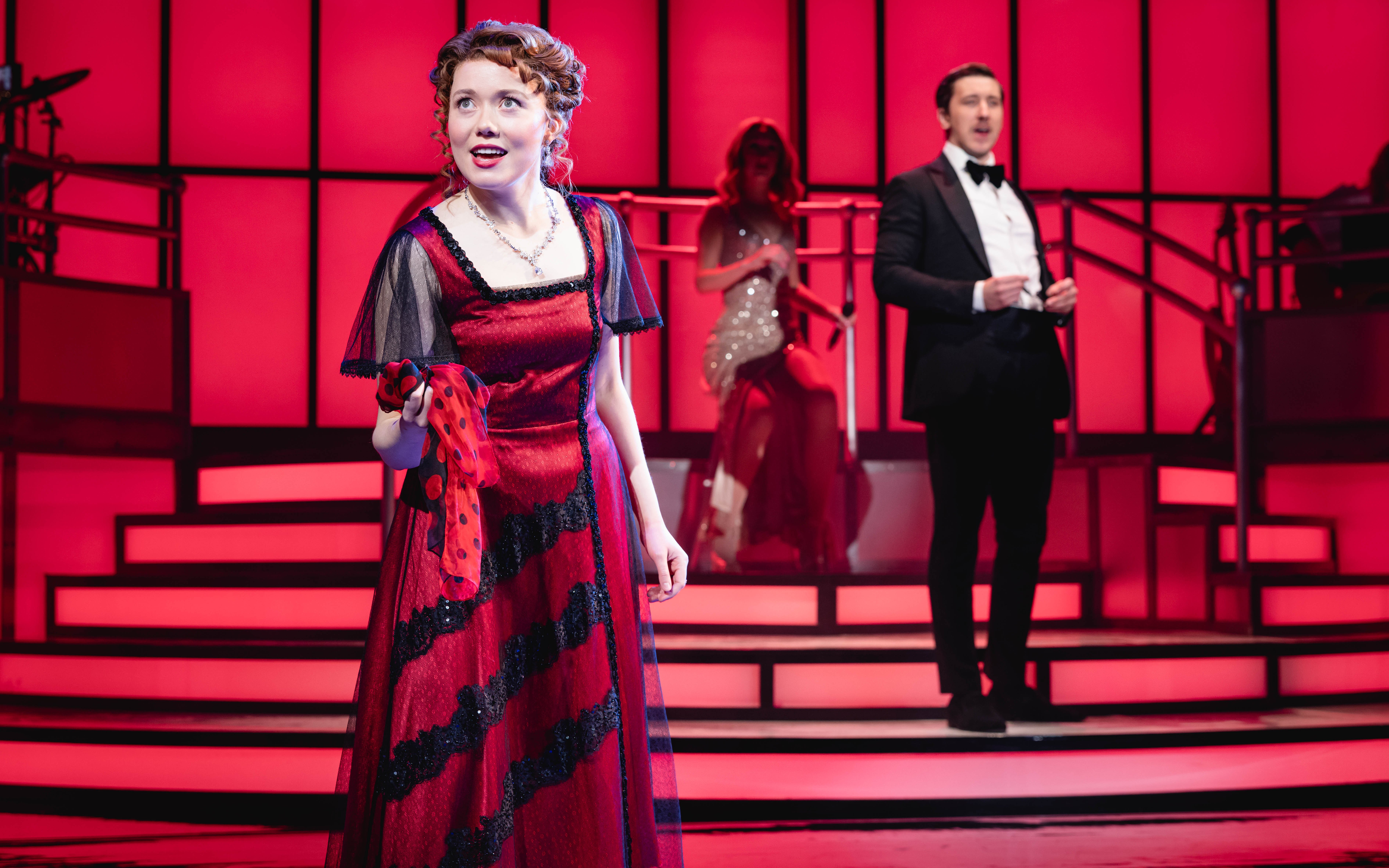 Stage performance of Titanique Westend with actors in period costumes on a red-lit set.