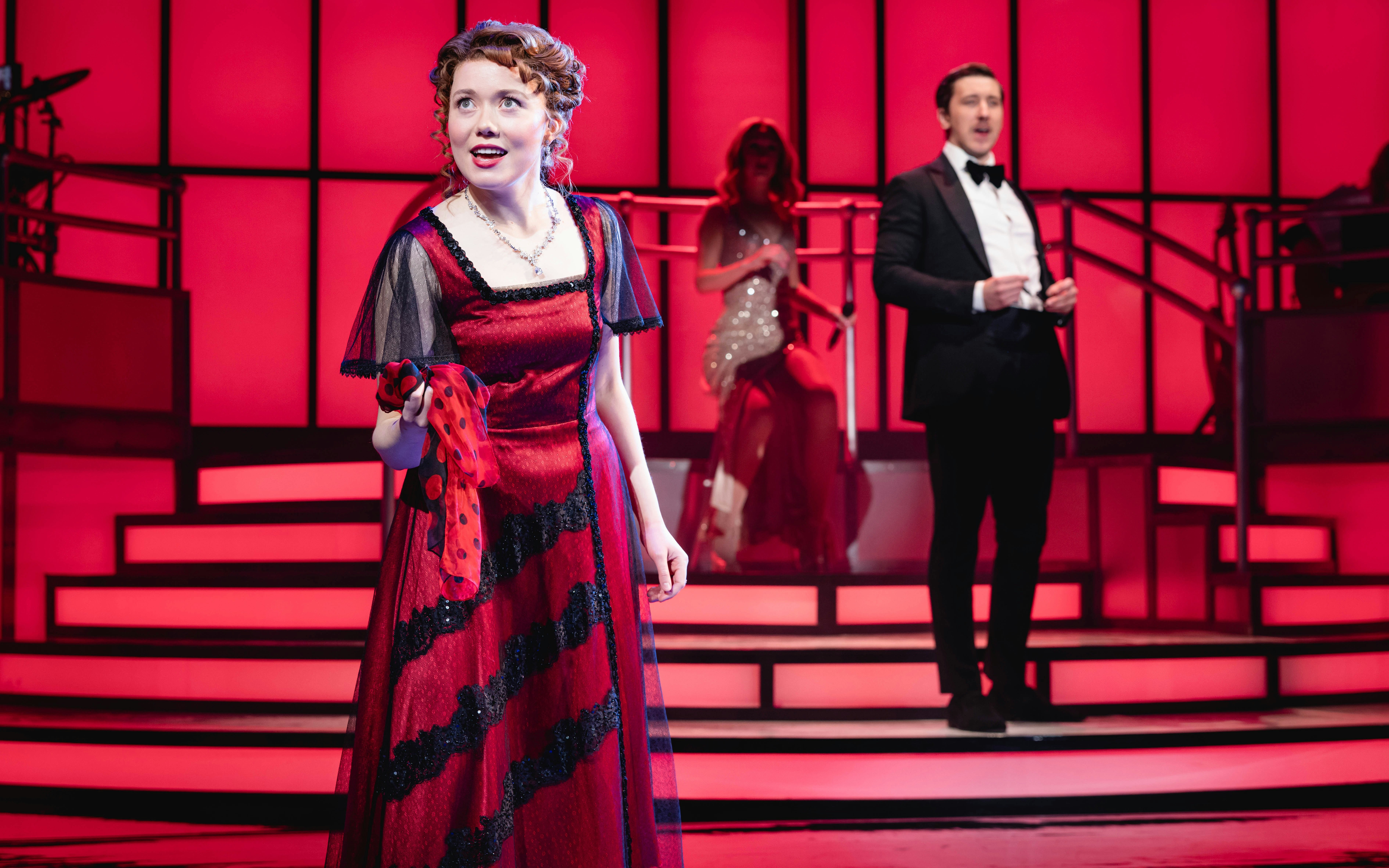 Stage performance of Titanique Westend with actors in period costumes on a red-lit set.