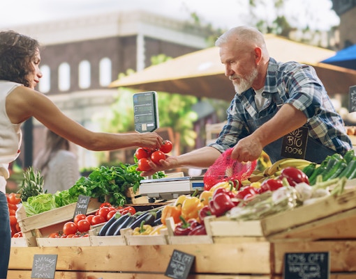 Vendor handing tomatoes to customer at Orlando Farmers’ Market.