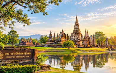 Sukhothai Historical Park with ancient temples and Buddha statues, reflecting in a pond.