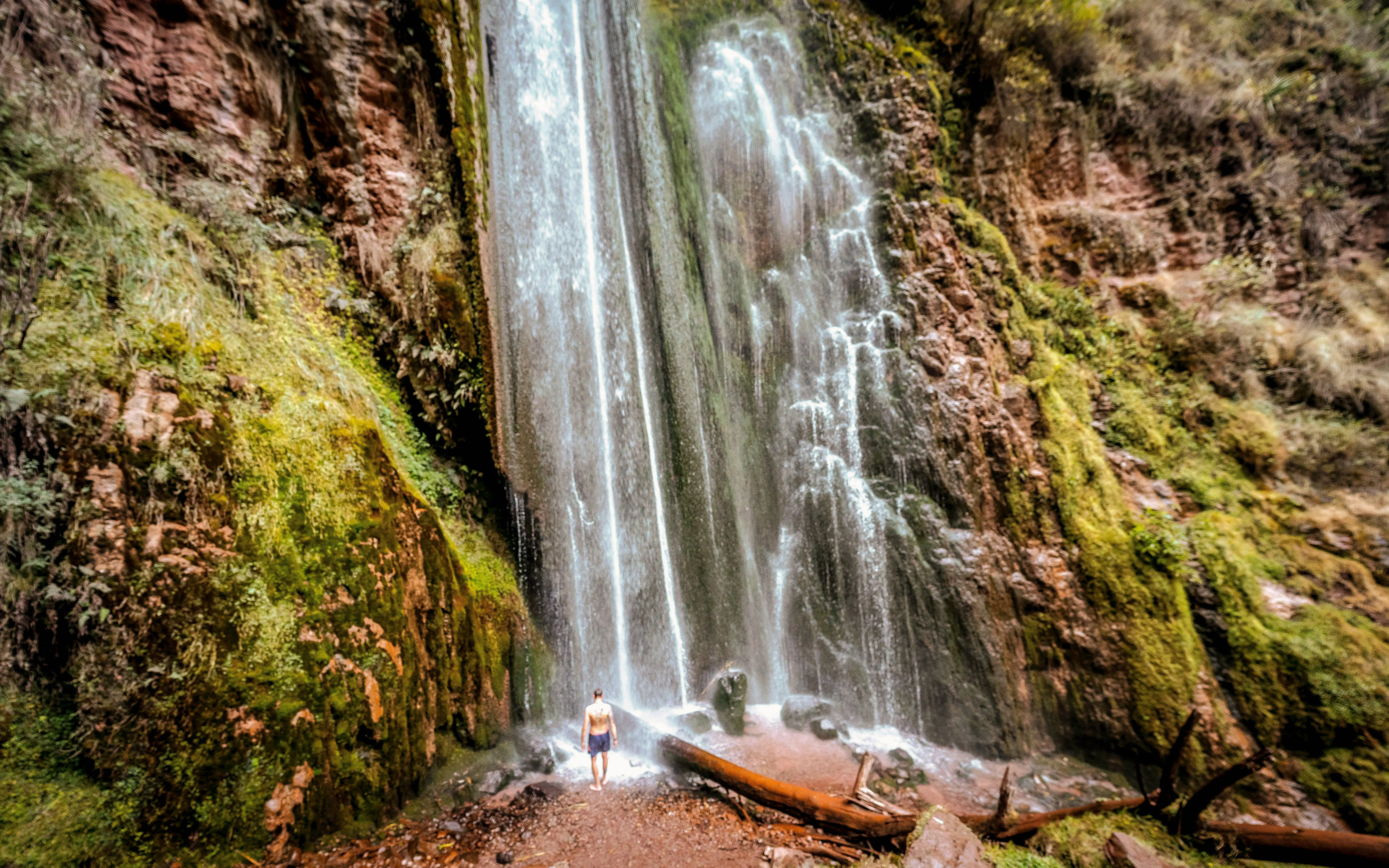 Person standing at the base of Perolniyoc waterfall in Ollantaytambo, Peru.