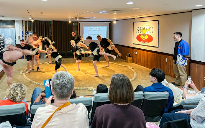 Tourists practicing sumo exercises with wrestlers in a Tokyo dojo.