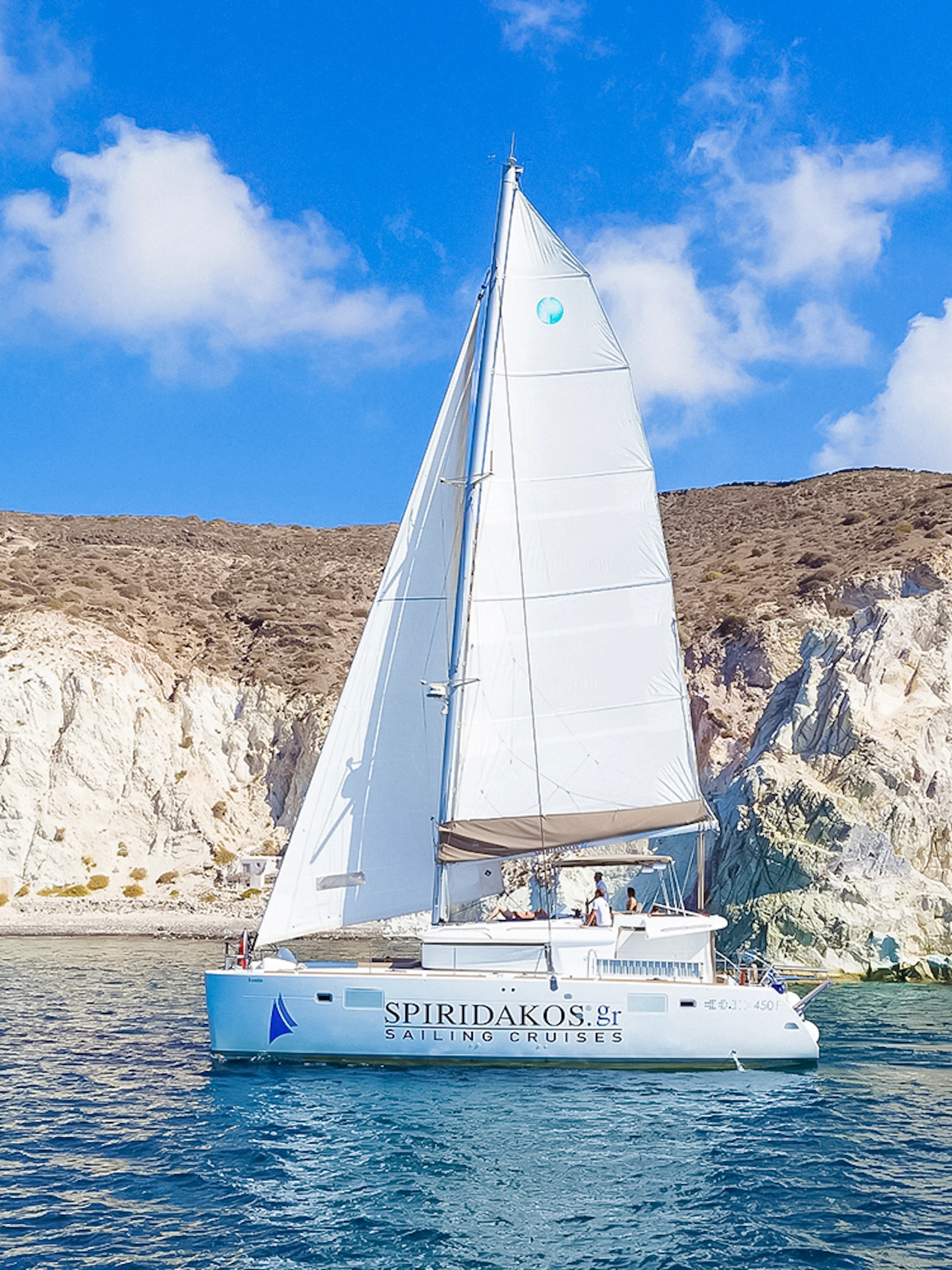 Catamaran sailing near rocky cliffs on a Santorini luxury cruise.