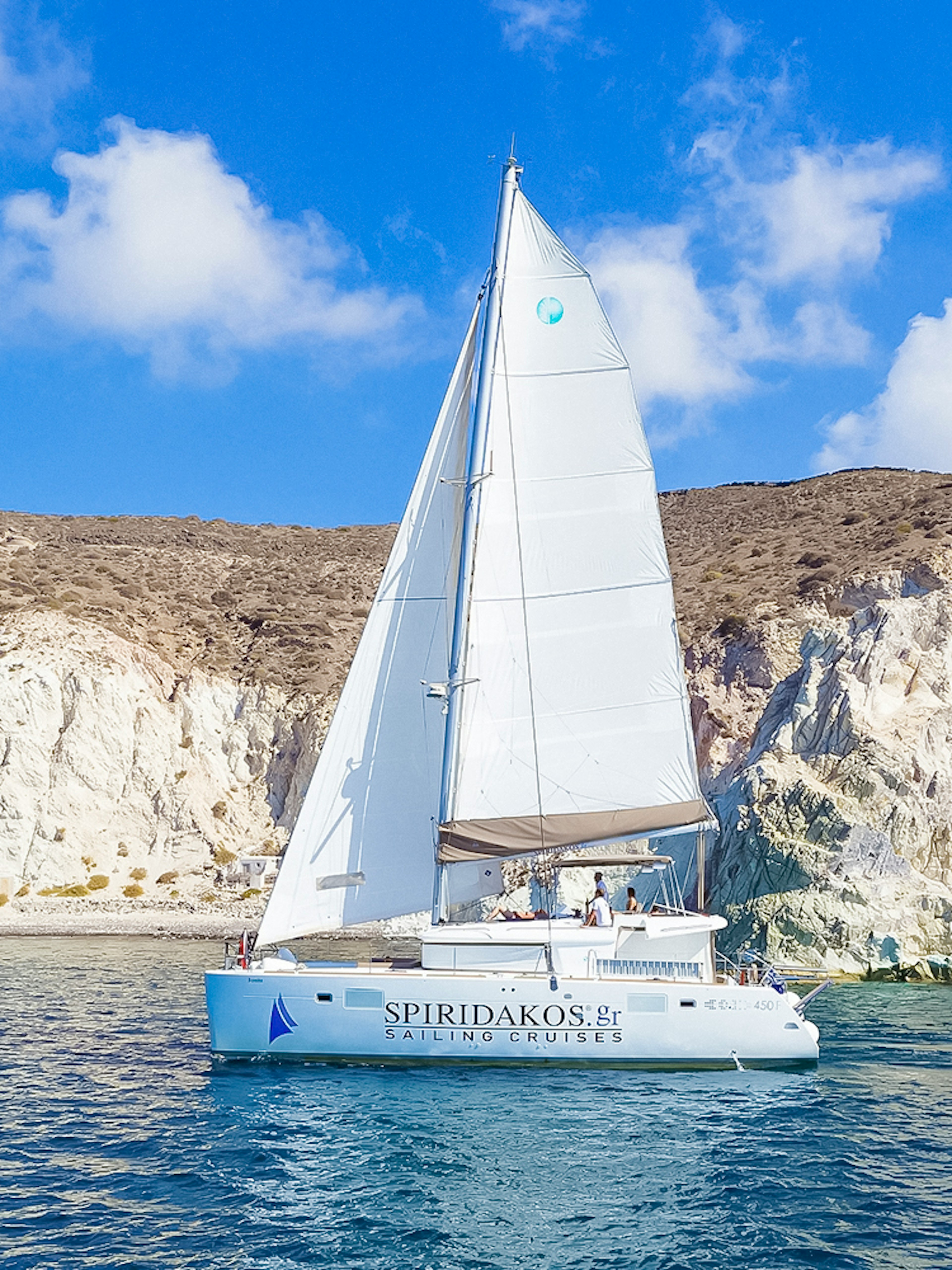 Catamaran sailing near rocky cliffs on a Santorini luxury cruise.