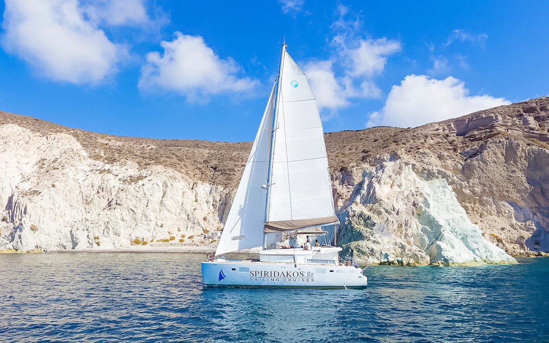 Catamaran sailing near rocky cliffs on a Santorini luxury cruise.