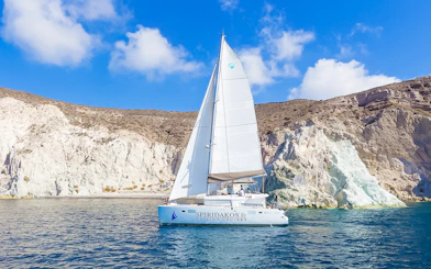 Catamaran sailing near rocky cliffs on a Santorini luxury cruise.