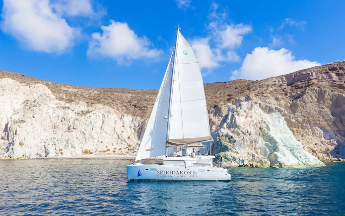 Catamaran sailing near rocky cliffs on a Santorini luxury cruise.