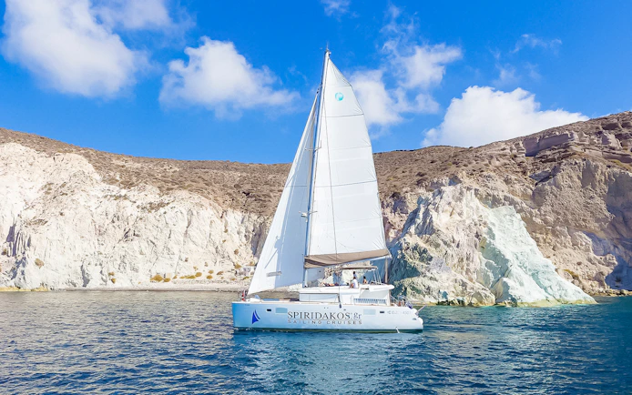 Catamaran sailing near rocky cliffs on a Santorini luxury cruise.
