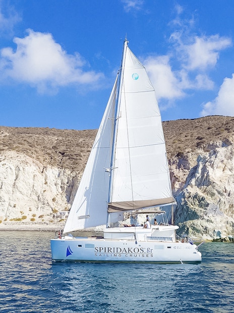 Catamaran sailing near rocky cliffs on a Santorini luxury cruise.