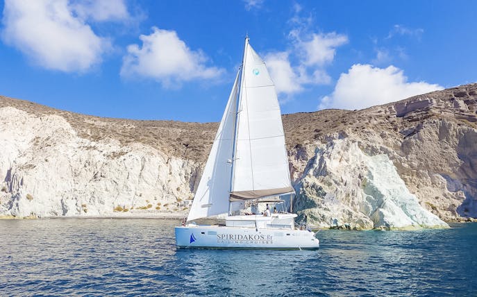 Catamaran sailing near rocky cliffs on a Santorini luxury cruise.