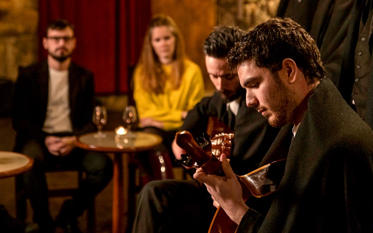 Musician playing guitar at Fado Maior with audience in Lisbon.