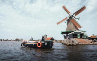 Boat passing by a traditional windmill at Zaanse Schans, Netherlands.