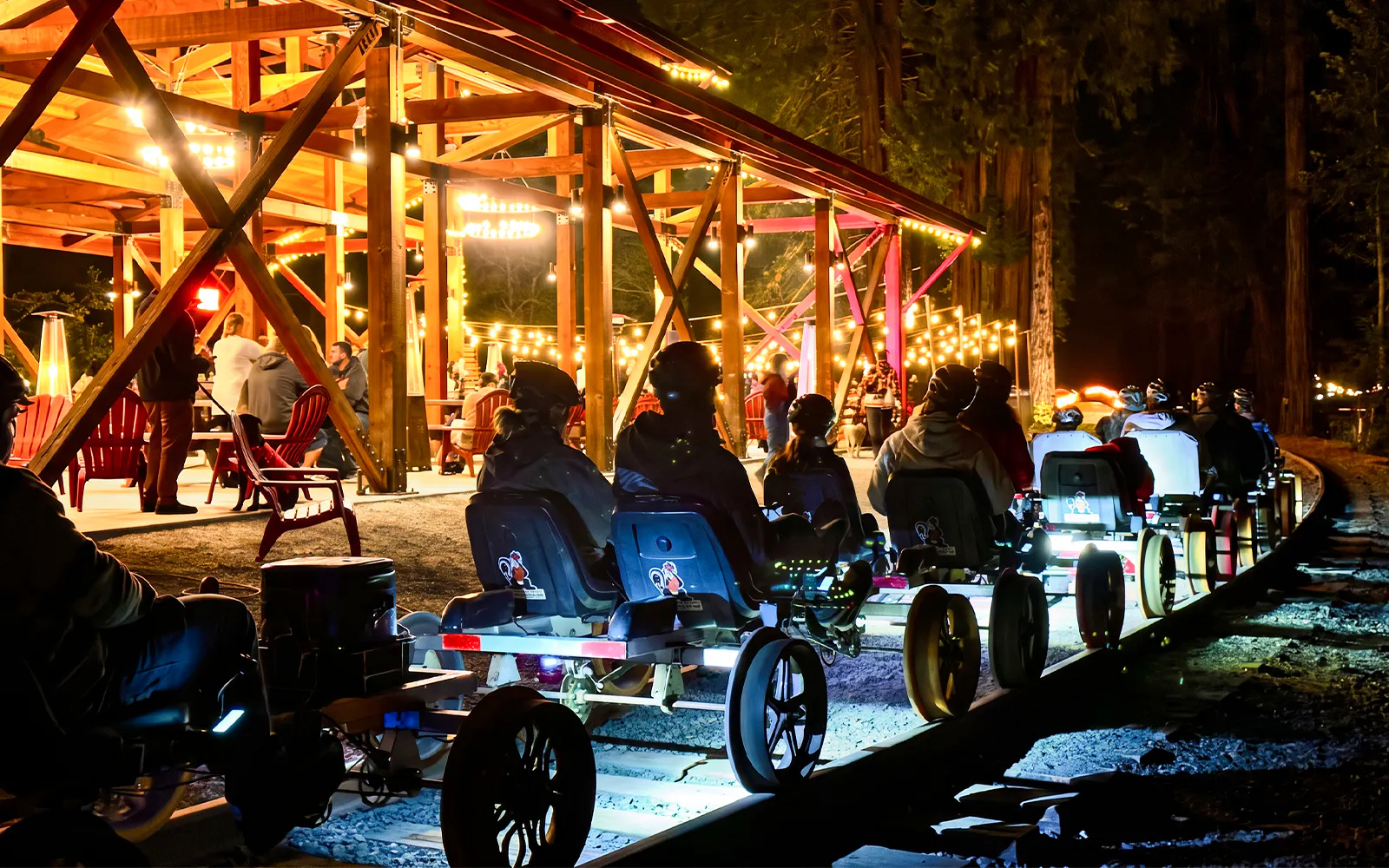 Visitors on rail bikes near Glen Blair Bar, San Francisco, illuminated by string lights at night.