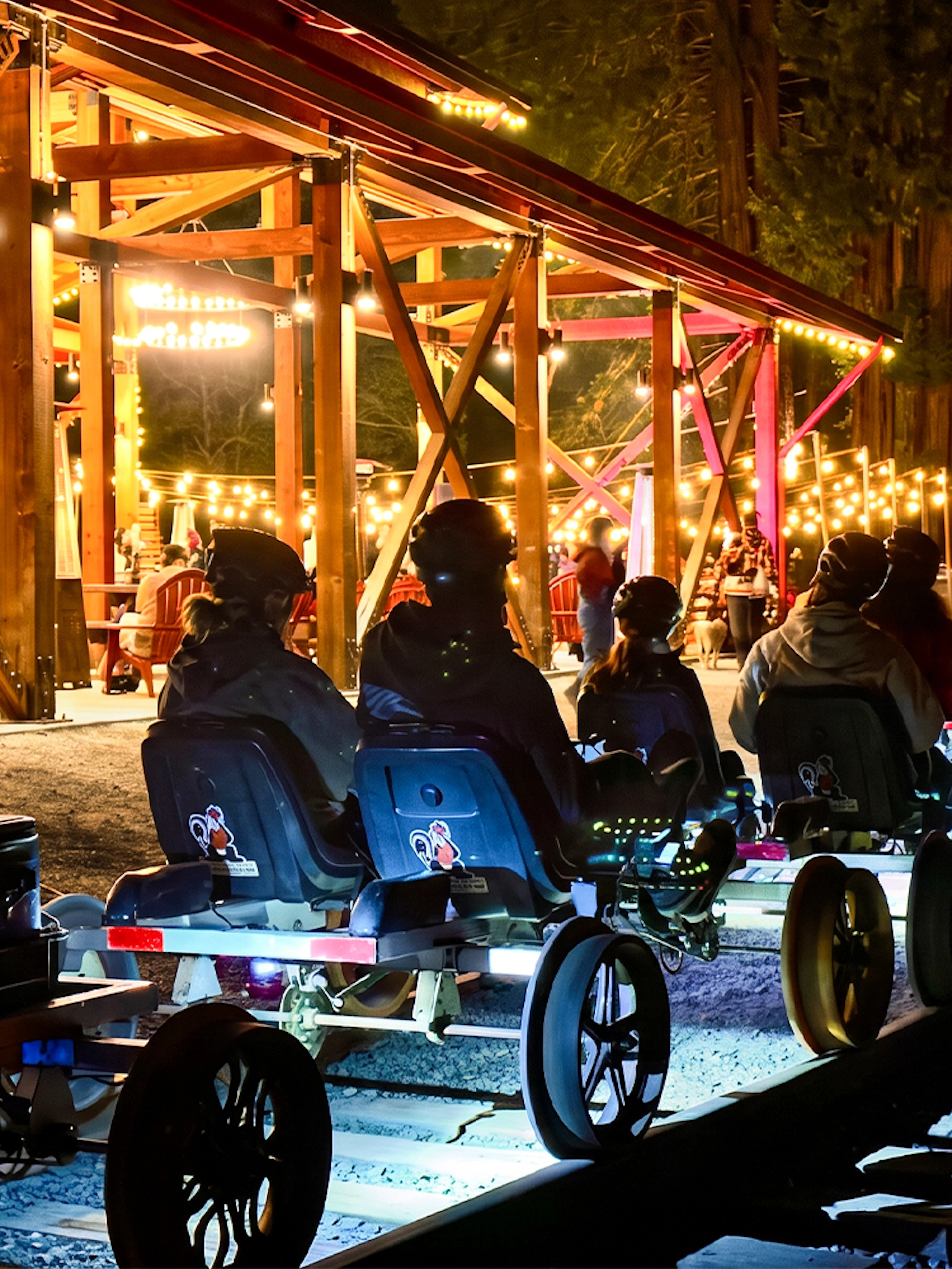 Visitors on rail bikes near Glen Blair Bar, San Francisco, illuminated by string lights at night.